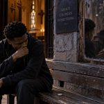A man outside a chapel seeing a mysterious hooded figure reflected in a mirror for Judas Mirror by K.P.M.
